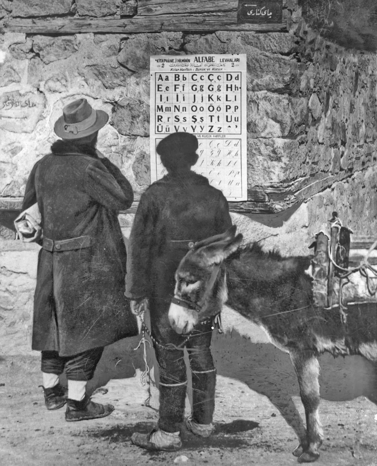 1928’de bir belediye binası önünde yeni Latin harflerini gösteren alfabe levhasına bakan iki kişi